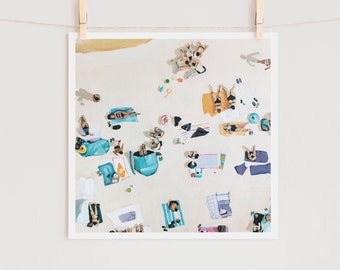May include: An aerial view of a beach scene with people sunbathing on towels and in the sand. The beach is white sand and the water is blue. There are colorful beach umbrellas and towels.