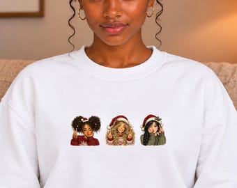 Può includere: Una felpa bianca a girocollo con una stampa grafica di tre figure illustrate che indossano cappelli da Babbo Natale rossi e bianchi. Ogni figura ha un'acconciatura diversa e indossa un maglione natalizio, due fanno il segno di vittoria.