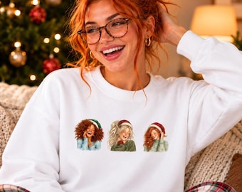 Può includere: Una felpa bianca a girocollo con una stampa grafica di tre figure illustrate che indossano cappelli da Babbo Natale. Le figure presentano acconciature e colori di capelli distinti, tra cui castano, biondo e rosso.
