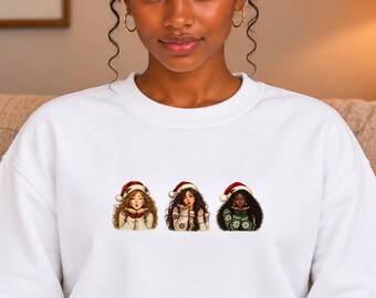 Può includere: Una felpa bianca a girocollo con una stampa grafica di tre figure illustrate che indossano cappelli da Babbo Natale e maglioni invernali a motivi. Ogni figura manda un bacio, con diverse texture e colori di capelli.