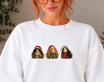Può includere: Una felpa bianca a girocollo con una stampa grafica di tre figure illustrate che indossano cappelli da Babbo Natale rossi e bianchi. Le figure hanno colori di capelli distinti e indossano abiti invernali, tra cui un maglione verde.