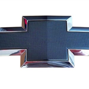 May include: A chrome and black Chevrolet emblem in the shape of a cross. The emblem has a black textured center and a shiny chrome border. The emblem is a car accessory.