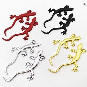 May include: A selection of lizard-shaped ornaments in red, black, silver, and gold. The image displays pairs of each colour, with detailed feet and long tails. These decorative lizards are ideal for adding a unique touch to any surface.