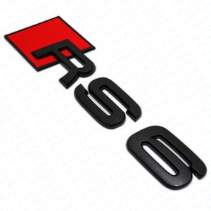 May include: Black and red RS emblem. The emblem features the letters "RS" in black, with a red square background. The emblem is designed to be affixed to a vehicle.