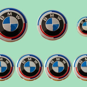 May include: A selection of BMW emblem decals. The circular decals feature the BMW logo in blue, white, and black, with a red and blue border. The background is a pale green.