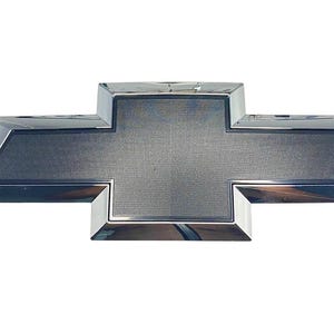 May include: A chrome Chevrolet emblem in the shape of a cross. The emblem has a textured, gray center and a shiny, reflective border. The emblem is isolated on a white background.