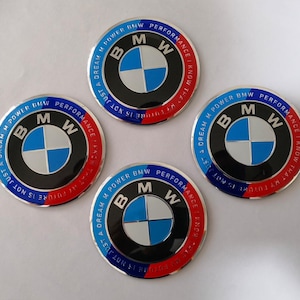 May include: Four circular BMW emblems. Each emblem features the BMW logo in the centre, a blue and white quadrant design, surrounded by a black ring. The outer ring is split into blue and red sections with white text.