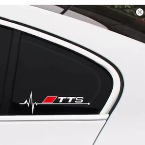 Könnte beinhalten: Weißes Autofenster mit schwarzer Tönung und einem weißen Aufkleber. Der Aufkleber zeigt eine Herzschlaglinie und die Buchstaben "TTS" in Weiß mit einem roten Quadrat. Das Auto ist weiß.