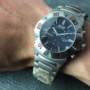 May include: A stainless steel Sector watch with a dark blue face and silver hands. The watch features a chronograph, sapphire crystal, and is water-resistant to 100 meters. The watch is on a stainless steel band.