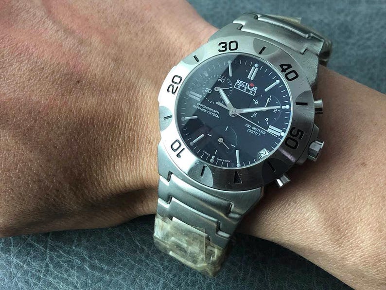 May include: A stainless steel Sector watch with a dark blue face and silver hands. The watch features a chronograph, sapphire crystal, and is water-resistant to 100 meters. The watch is on a stainless steel band.