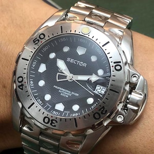 May include: A silver Sector Professional Diver automatic wristwatch with a black dial. The watch features a date display at the 3 o'clock position and a rotating bezel with minute markers. The watch is water resistant to 200 meters.