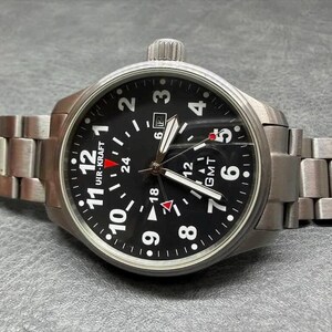 May include: A stainless steel wristwatch with a black dial, featuring white Arabic numerals, a date window, and a GMT function. The watch has a brushed metal link bracelet, a crown at the top, and the text UHR-KRAFT printed on the watch face.