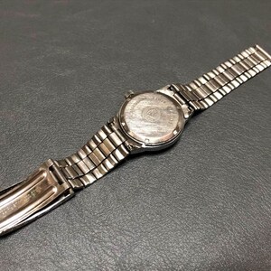 Puede incluir: Un reloj de pulsera plateado con una correa de metal, visto desde atr&aacute;s, sobre una superficie oscura. La esfera del reloj es visible y la correa est&aacute; parcialmente abierta. El reloj tiene un dise&ntilde;o cl&aacute;sico y vintage.