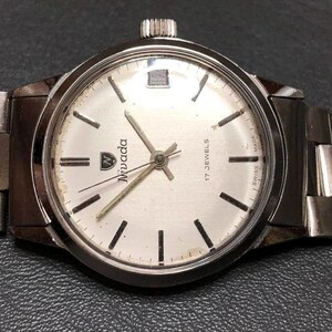 Puede incluir: Reloj de pulsera Nivada plateado con esfera blanca, marcadores de hora negros y agujas plateadas. El reloj tiene una correa de acero inoxidable y una corona a las 3 en punto. La esfera del reloj dice "Nivada" y "17 Jewels Swiss Made".