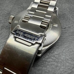 May include: A silver-toned stainless steel wristwatch featuring a metal link bracelet and a fold-over clasp engraved with the text UIR-KRAFT. The circular case back displays the text 5ATM, indicating water resistance, along with other markings.