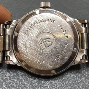 Puede incluir: Primer plano de la parte trasera de un reloj de pulsera plateado con una correa de acero inoxidable. La esfera del reloj es circular con las palabras "WATER RESISTANT" y "STAINLESS STEEL" grabadas. El reloj tambi&eacute;n tiene el n&uacute;mero "47011" grabado.