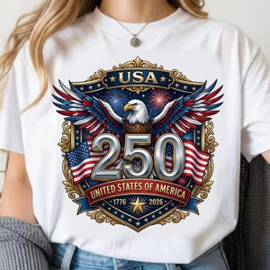 May include: White t-shirt featuring a patriotic design celebrating the 250th anniversary of the United States. The graphic includes an eagle, American flags, fireworks, and the text "USA", "250", and "United States of America 1776-2026".