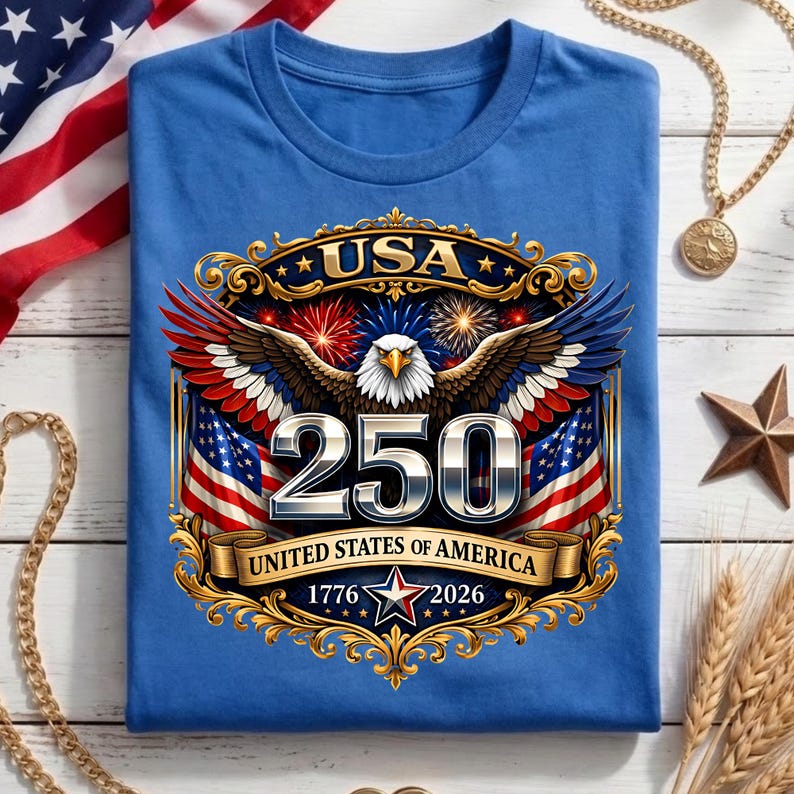 May include: A blue t-shirt featuring a patriotic design with an eagle, American flags, and the text "USA 250 UNITED STATES OF AMERICA 1776-2026". The design incorporates red, white, and blue colors with gold accents.
