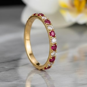 May include: A gold ring with alternating red and white gemstones. The ring has a continuous row of small, round rubies and diamonds set in a yellow gold band. The gemstones are evenly spaced around the ring.