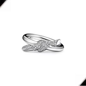 K&ouml;nnte beinhalten: Ein silberfarbener Ring mit Knoten-Design. Der Knoten ist mit kleinen, funkelnden Edelsteinen besetzt. Der Ring hat eine polierte, reflektierende Oberfl&auml;che, vor wei&szlig;em Hintergrund.
