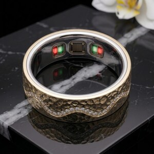May include: A gold-toned smart ring featuring a textured, hammered exterior surface with a wavy channel of small, clear stones. The interior band displays electronic sensors with visible red and green lights and a central metallic contact grid.