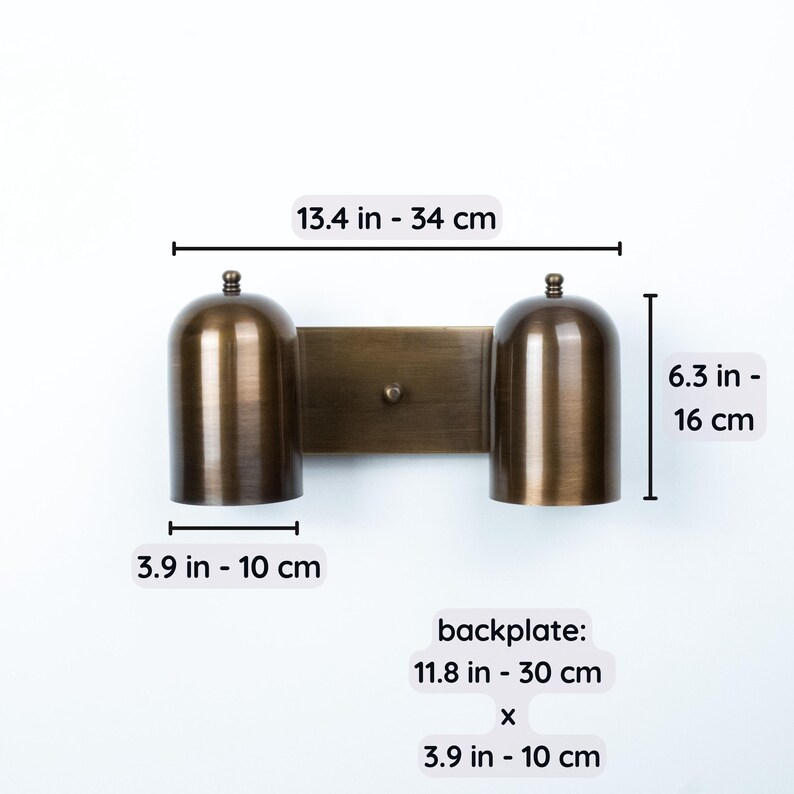 May include: A double-light wall sconce in a brushed bronze finish with two dome-shaped shades. The fixture measures 13.4 inches wide by 6.3 inches high, with 3.9-inch wide shades and a backplate measuring 11.8 inches by 3.9 inches.