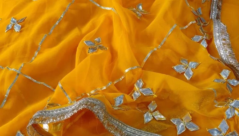 May include: A vibrant yellow fabric with intricate silver embellishments. The fabric is adorned with silver floral-shaped accents and silver trim along the edges, creating a luxurious and decorative textile.