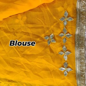 May include: A close-up of a yellow blouse with decorative silver and gold embellishments. The blouse has a delicate, sheer texture. The word "Blouse" is printed in white on the left side of the image.