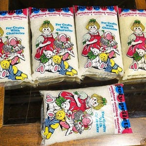 May include: Five clear plastic bags of Poly-Pellets weighted stuffing material. Each bag features a graphic of a child with a doll and two teddy bears, with the text For Crafts With Character and a net weight of 12 ounces or 340 grams.