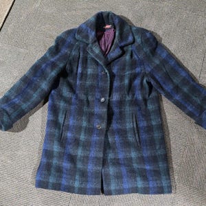 May include: A blue and green checked coat with a button-up front and a collar. The coat has long sleeves and a purple lining. The coat is made of a textured fabric.