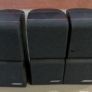 May include: Set of six black Bose cube speakers. Each speaker has a textured fabric cover and a red accent line. The Bose logo is visible on the bottom of each speaker.