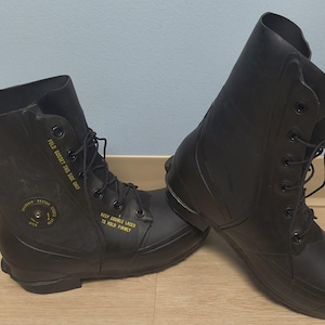 May include: A pair of black rubber lace-up boots featuring yellow printed text that reads FOLD GUSSET THIS SIDE ONLY and KEEP DOUBLE LACED TO HOLD FIRMLY. The boots include a circular valve-like detail on the side with the text INFLATION SYSTEM.