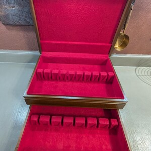 May include: Wooden cutlery storage box with a red velvet interior. The box has two levels with slots for utensils. The exterior is a dark brown colour with a brass handle. A brass ladle hangs on the side.