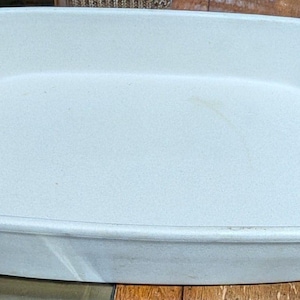 May include: A rectangular, off-white ceramic baking dish with rounded corners. The dish has a slightly textured surface and a raised rim. The interior is smooth and clean, suggesting it's ready for use. The dish is likely for baking casseroles or other dishes.