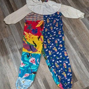 Puede incluir: Un colorido disfraz de payaso con cuello con volantes blanco y mangas largas. Los pantalones de patchwork presentan patrones vibrantes que incluyen diseños florales, geométricos y de dibujos animados. El disfraz está diseñado para un look juguetón y caprichoso.