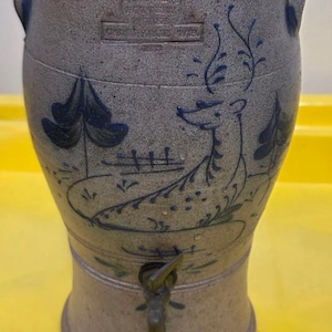 Könnte beinhalten: Ein Wasserkühler aus Steinzeug mit einem Hirsch- und Landschaftsdesign in Blau. Der Kühler hat einen Wasserhahn und zwei Griffe. Er ist 20 cm breit, 20 cm lang und 36 cm hoch.