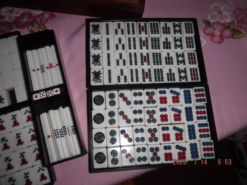 May include: A set of mahjong tiles in a black case. The tiles are white with black and red markings. The tiles are arranged in a grid pattern. The case has a black background with white lettering. The tiles are arranged in a grid pattern. The case has a black background with white lettering. The tiles are arranged in a grid pattern. The case has a black background with white lettering.