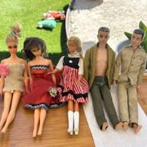 May include: Five dolls arranged in a row. The first wears a cream dress, the second a red dress with black trim, the third a red and white striped dress with a black bodice, the fourth a tan jacket and green pants, and the fifth a tan shirt and pants.