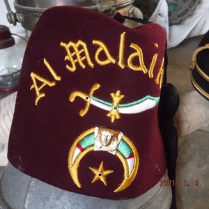 May include: A maroon fez with gold embroidery that reads "Al Malai" and features a crescent moon, star, and crossed swords.