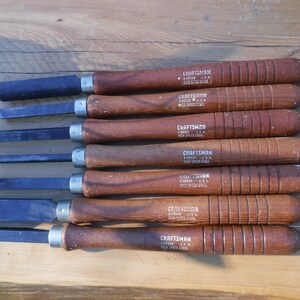 May include: Set of eight wood handled chisels with black metal blades. The handles are brown and have the text "CRAFTSMAN 3/32" and "HIGH SPEED STEEL" printed on them.
