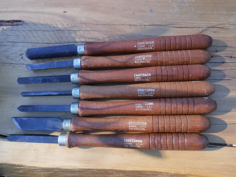 May include: Set of eight wood handled chisels with black metal blades. The handles are brown and have the text "CRAFTSMAN 3/32" and "HIGH SPEED STEEL" printed on them.