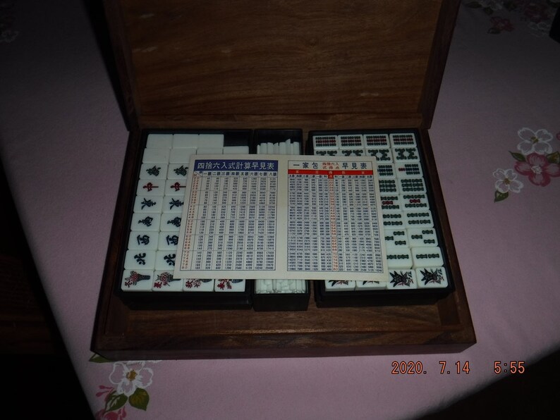 May include: A wooden box containing a set of white mahjong tiles with black characters and red accents. The box also includes two instruction cards with Chinese text and a set of white sticks. The box is closed.