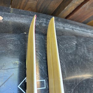 May include: Two vintage wooden skis with a red and white stripe down the center. The skis are yellowed with age and have a worn finish.