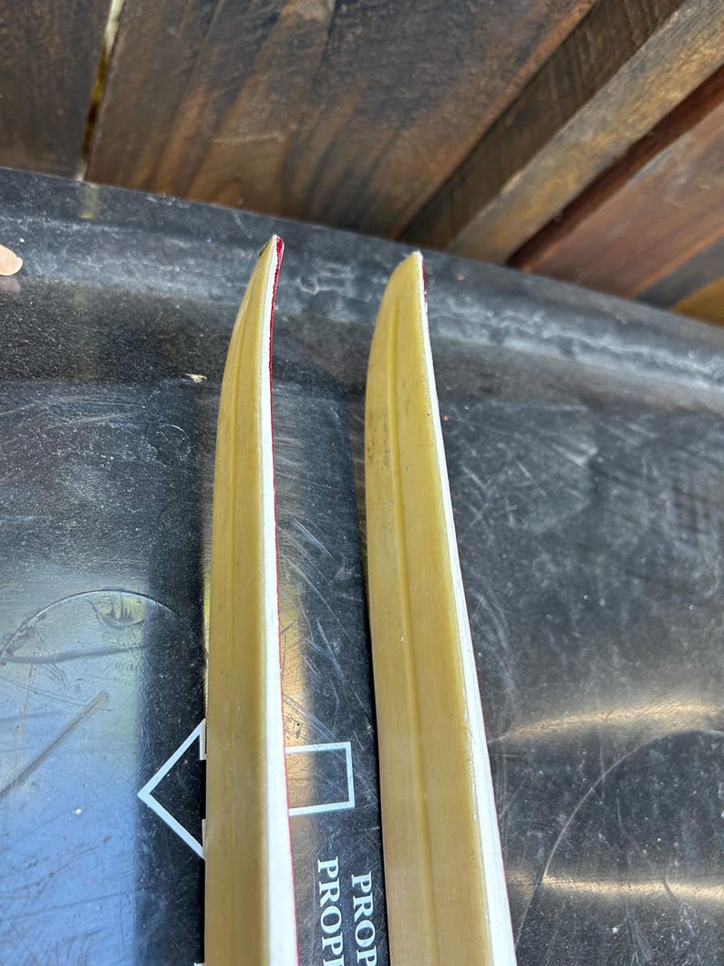 May include: Two vintage wooden skis with a red and white stripe down the center. The skis are yellowed with age and have a worn finish.