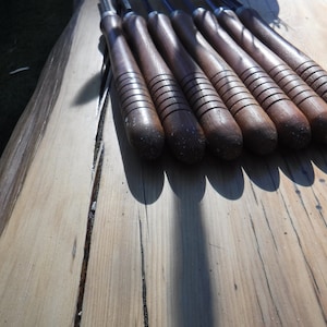 May include: A set of eight wood-handled carving tools with metal blades. The tools are arranged in a row on a wooden surface.