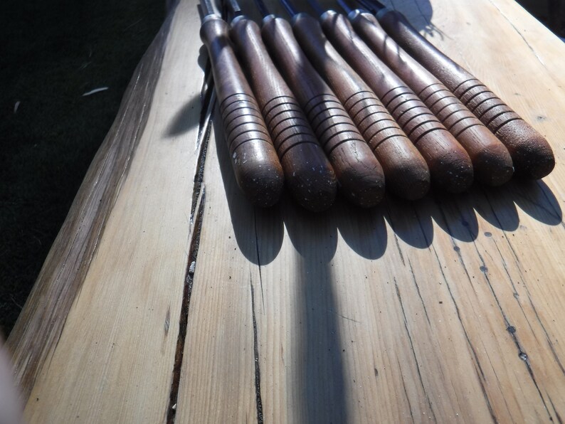 May include: A set of eight wood-handled carving tools with metal blades. The tools are arranged in a row on a wooden surface.