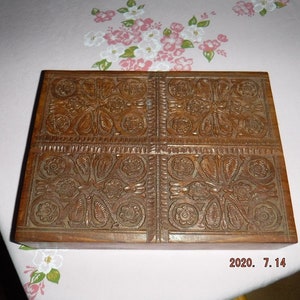 May include: A wooden box with intricate carved floral designs on the top. The box is made of dark brown wood and has a rectangular shape.