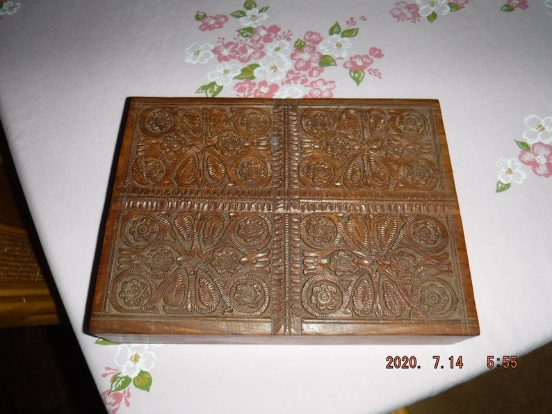 May include: A wooden box with intricate carved floral designs on the top. The box is made of dark brown wood and has a rectangular shape.