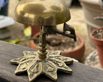 May include: A brass bell with a star-shaped base and a decorative handle. The bell is polished and has a shiny finish.