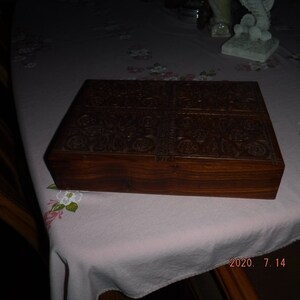 May include: A dark brown wooden box with intricate carvings on the top and sides. The box has a hinged lid and is closed.